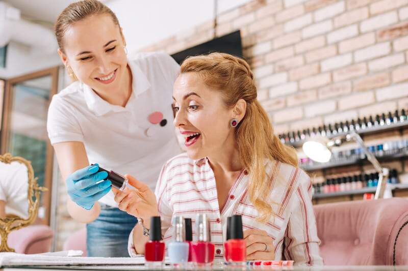 Contabilidade para manicures - Imagem de profissional de beleza e sua cliente no salão de manicure escolhendo esmaltes